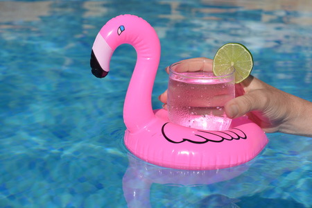 Hand holding a drink in an inflatable pink flamingo drinks holder in swimming pool