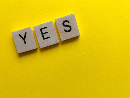 The word Yes in wooden letters on a bright yellow textured background with copy spaceの写真素材