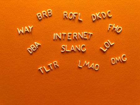 Internet slang, acronyms including ROFL, (Rolling on floor laughing) LOL (Lots of Laughs), LMAO, TLTR, DBA, WAY, BRB, in alphabet letters on a bright orange background with copy spaceの写真素材