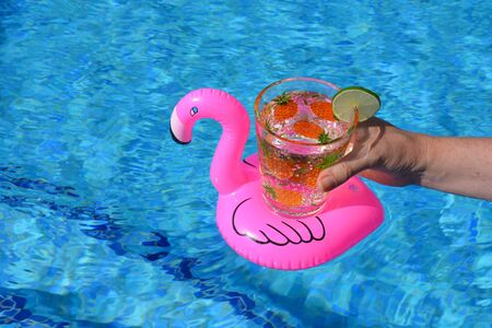 Woman holding glass decorated with pineapples, of sparkling water with a slice of lime, in a pink...