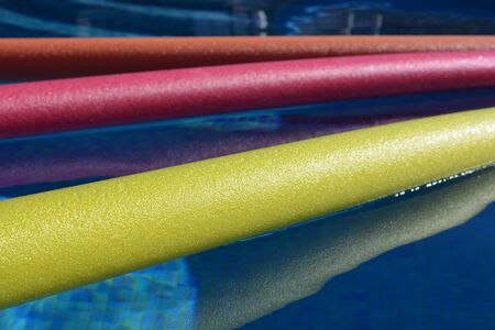 Bright yellow, pink and orange pool noodles, floating in a swimming pooの写真素材