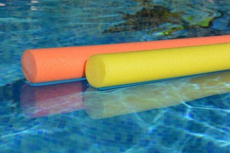 Bright yellow, pink and orange pool noodles, floating in a swimming pool