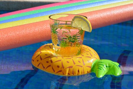 Glass of water in an inflatable pineapple drinks holder and pool noodles floating in a swimming...