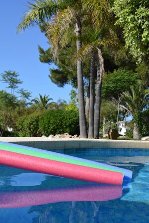 Pool noodles on poolside in a Mediterranean garden