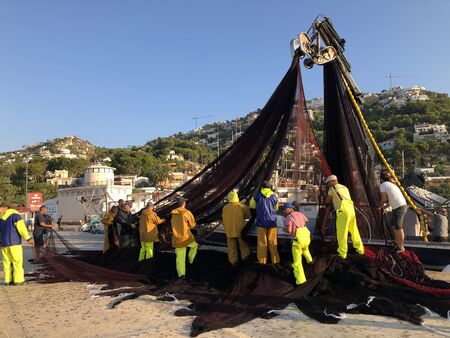 Fishermen in oilskins sorting and cleaning  the trawling nets from their boat on return to port early in the morning,, Javea, Alicante Province, Spainのeditorial素材