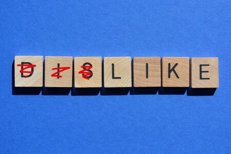 Dislike, with prefix dis crossed out, leaving the word Like, in 3d wooden alphabet letters isolated on blue background.の写真素材