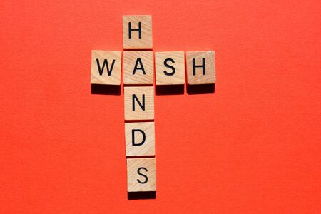Wash Hands, words in 3d wooden alphabet letters in crossword form isolated on red backgroundの写真素材