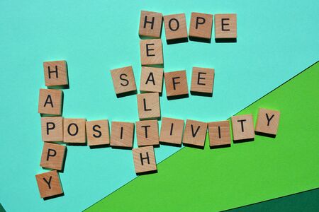 Positivity, Happy, Healthy, Safe, Hope, words in 3d wooden alphabet letters in crossword form isolated on green backgroundの写真素材