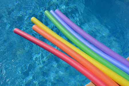 Rainbow coloured pool noodles floating in a swimming pool on a bright and sunny day