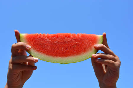 Young woman holding up a slice of juicy red watermelonの写真素材