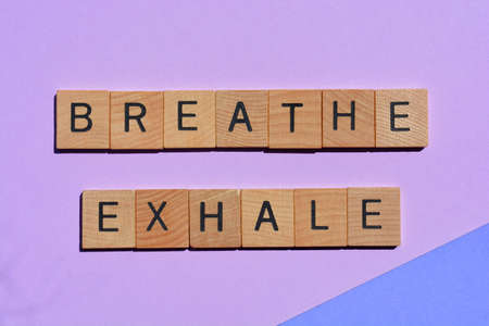 Breathe, Exhale, words in 3D wooden alphabet letters isolated on purple backgroundの写真素材