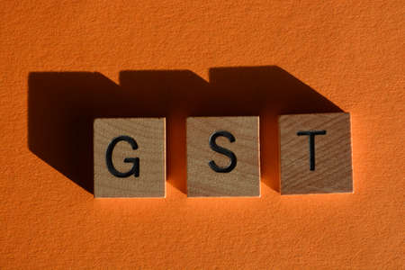 GST acronym for Goods and Services Tax, in wooden alphabet letters isolated on orange background