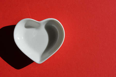 White ceramic heart shaped dish isolated on bright red background with copy spaceの写真素材