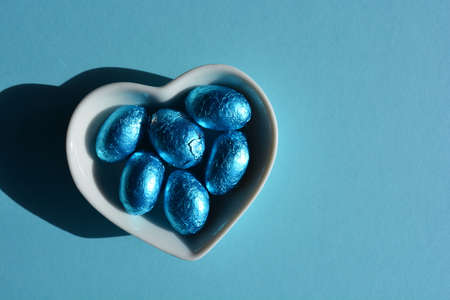 Blue foil wrapped chocolate Easter eggs in heart shaped dish isolated on backgroundの写真素材