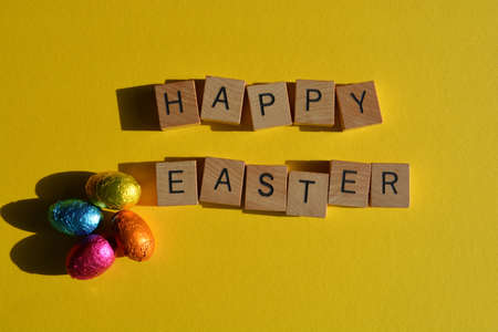 Happy Easter, words in wooden alphabet letters and foil wrapped chocolate eggs isolated on bright...