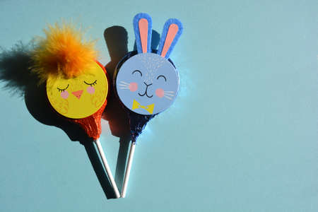 Easter themed chocolate lollipops, chick and bunny shapes isolated on blue background with copy...
