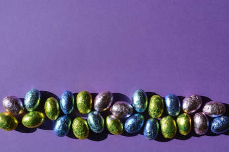 Foil wrapped chocolate Easter eggs isolate on purple background with copy space