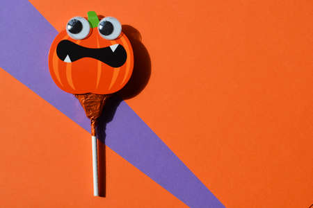 Halloween candy, pumpkin shaped lollipop with googly eyes on orange background with copy spaceの写真素材
