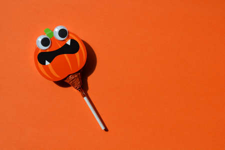 Halloween pumpkin shaped lollipop with googly eyes on bright orange background with copy spaceの写真素材