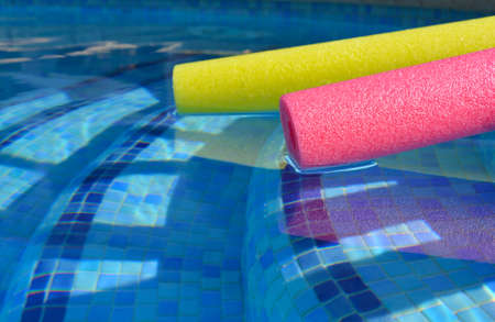 Swim noodles in blue tiled swimming pool, selective focus on pink polyethylene foamの写真素材