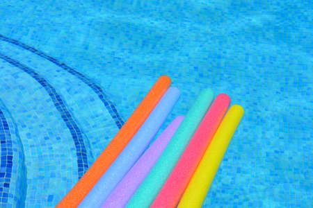 Rainbow colour swim noodles floating  on water of swimming pool. Summer fun