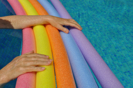 Rainbow coloured floating foam sticks and female hands, in swimming poolの写真素材