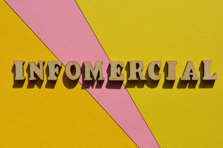 Infomercial, word blend of Information and Commercial, known as a portmanteau in wooden alphabet letters isolated on pink and yellow background as banner headlineの写真素材