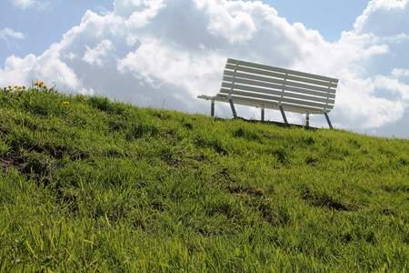 White bench stands on a green meadow on the horizon