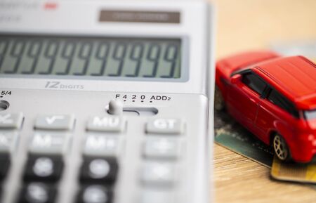Grey Calculator digital to calculate car finance and insurance and red car model lay on the brown...