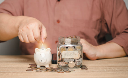 A man is calculating money to save and puts it in a piggy bank. Ideas for saving money for future home purchases and use in future after retirement. Family expenses.の写真素材