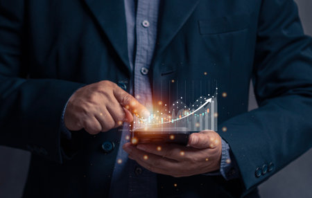 Businessman points at virtual screen of mobile phone at stock graph. The concept of stock trading via mobile phone. Financial stock exchange graph. Trade stock and bitcoin currency. Online trade.の写真素材