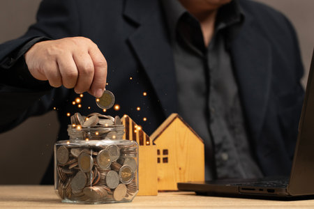 Man putting coins in a jar full of savings. The goal of real estate investing and using technology for financial management and informed decision making. Strategic planning and long term investment.の写真素材