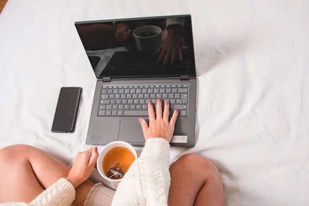 girl teleworking at home comfortably from bed or sofa with a cup of tea during virus pandemic