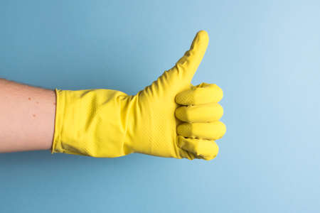 hand with yellow cleaning glove making okay gestures on a blue colored background. Cleaning and hygiene conceptの写真素材
