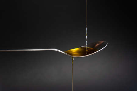 Spoon with extra virgin olive oil on black background. Golden olive oil. Mediterranean and healthy...