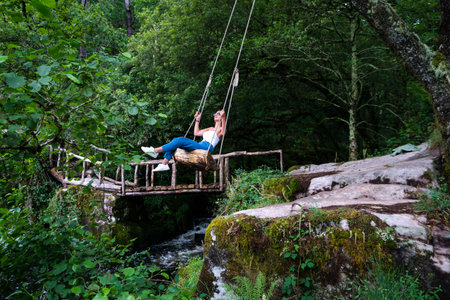 Girl on a swing over a river, inside a green forest in Galicia. Nature. Adventure.の写真素材