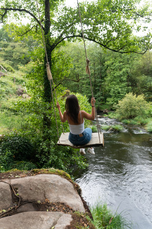 Girl on a swing over a river, inside a green forest in Galicia. Nature. Adventure.の写真素材