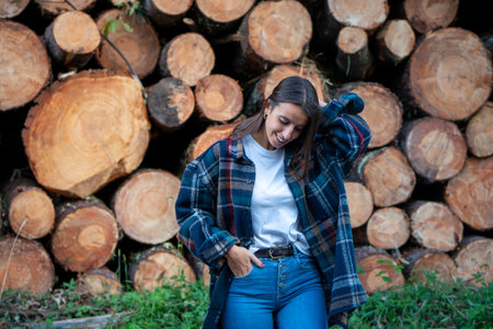 Young girl dressed in a lumberjack shirt next to some cut and stacked tree trunks. Concept environment, sustainability, nature, deforestation.の写真素材