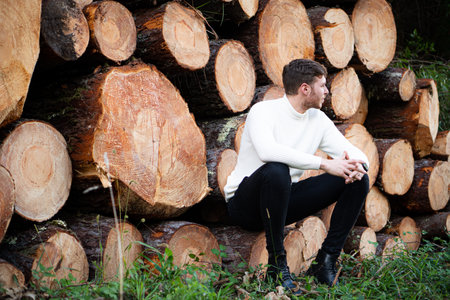 Young man with logs of wood stacked behind him. Concept construction, wood, deforestation, industry.