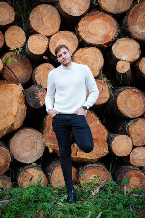 Young man with logs of wood stacked behind him. Concept construction, wood, deforestation, industry.の写真素材