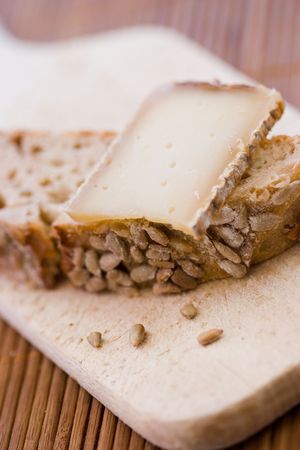 A french tasty slice of cheese on a piece of bread with cereals on a wooden board
