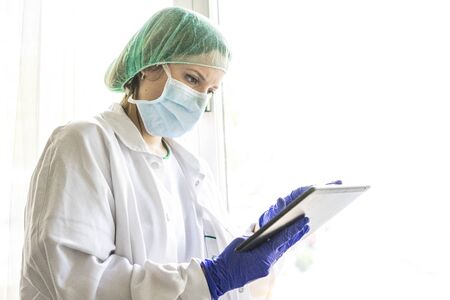Cropped shot of an unrecognizable female nurse using a digital tablet while standing in a hospital....