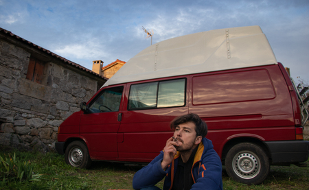 Young man smoking in front of his do it yourself red camper vanの写真素材