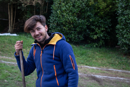 Young smiling in a rural setting, holding a wooden stick with vegetation on the backの写真素材