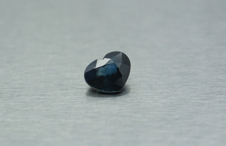Blue gemstone carved in the shape of a heart on gray metallic backgroundの写真素材