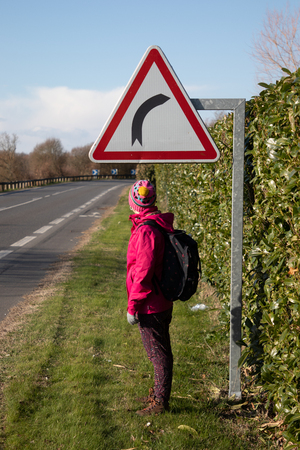 Girl hiking under a curve sign on the road wearing pink coatの写真素材