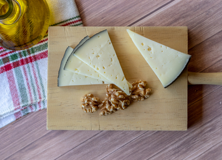Tasty cheese on a rustic table accompanied by healthy peeled walnuts and a glass bottle of extra virgin olive oilの写真素材