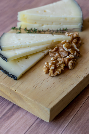 Tasty cheese on a table with nuts and fresh thyme branches. Rustic mediterranean appetizer table with manchego cheese.の写真素材