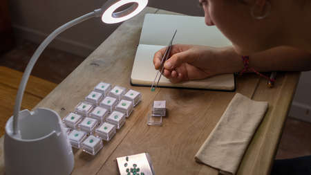 Geologist woman working at her desk looking at a precious stone in a lamp. Workspace with jewelry tools.の写真素材