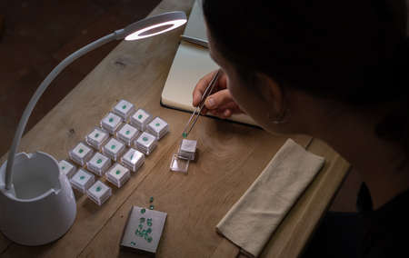 Gemologist woman working at her desk looking at a precious stone in a lamp. Workspace with jewelry tools.の写真素材